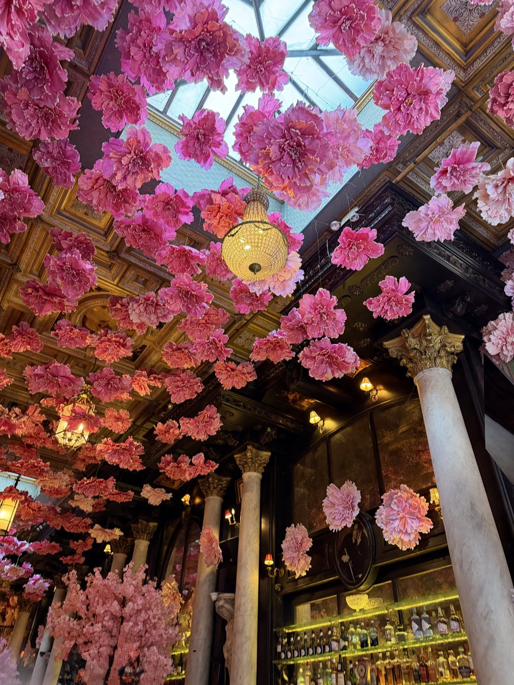 Pink paper flowers hanging from an ornate bar ceiling in New York City